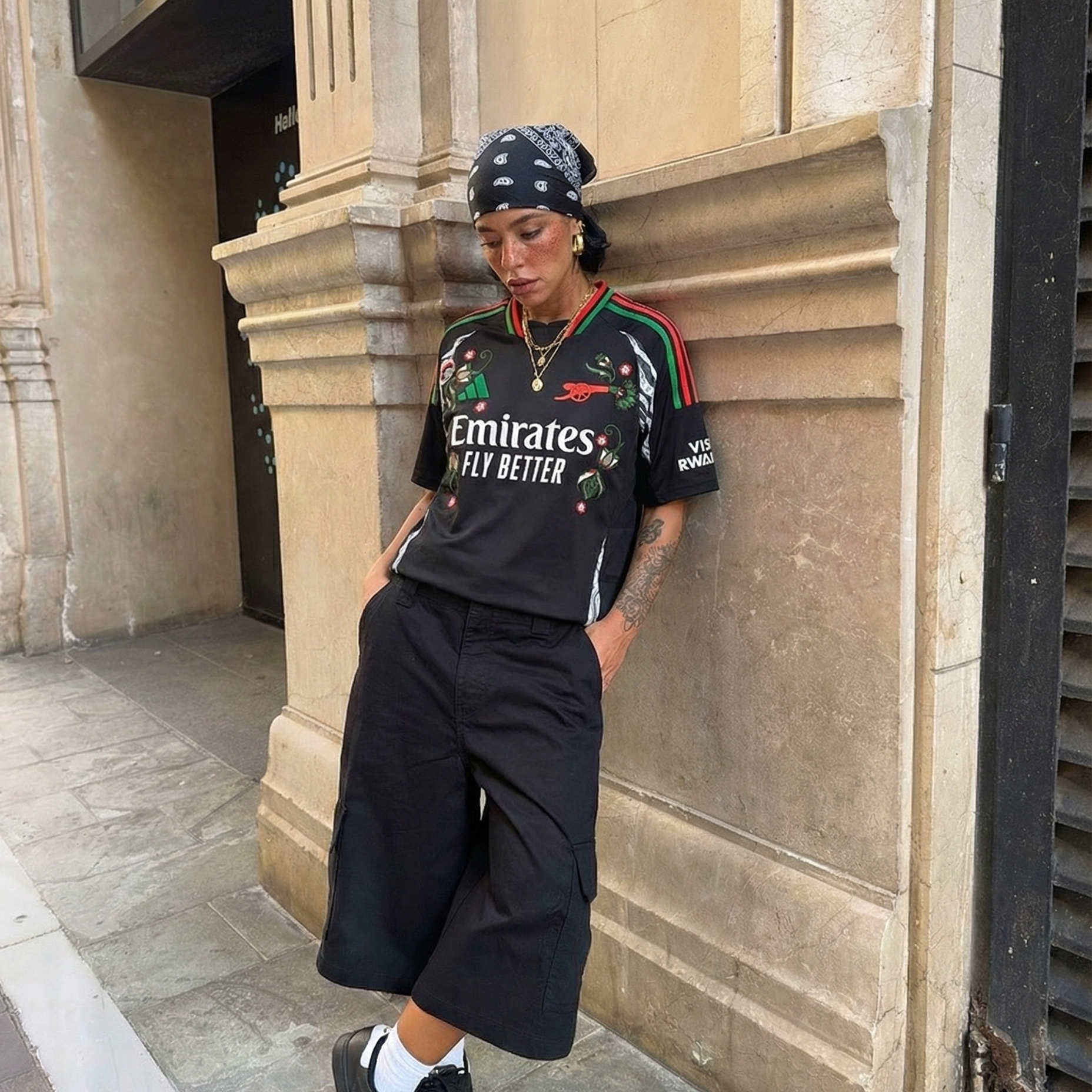 Person wearing Arsenal away football jersey with floral embroidery, black shirt styled with loose black pants in an urban streetwear setting
