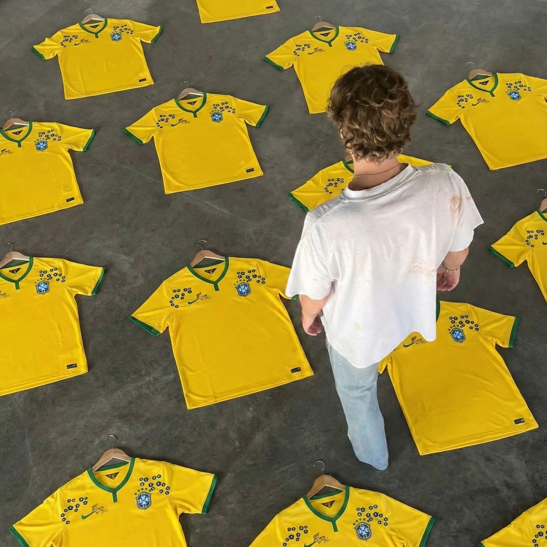 Multiple Brazil 2014 home football jerseys with floral details laid on the floor, yellow shirts arranged symmetrically with a person standing among them