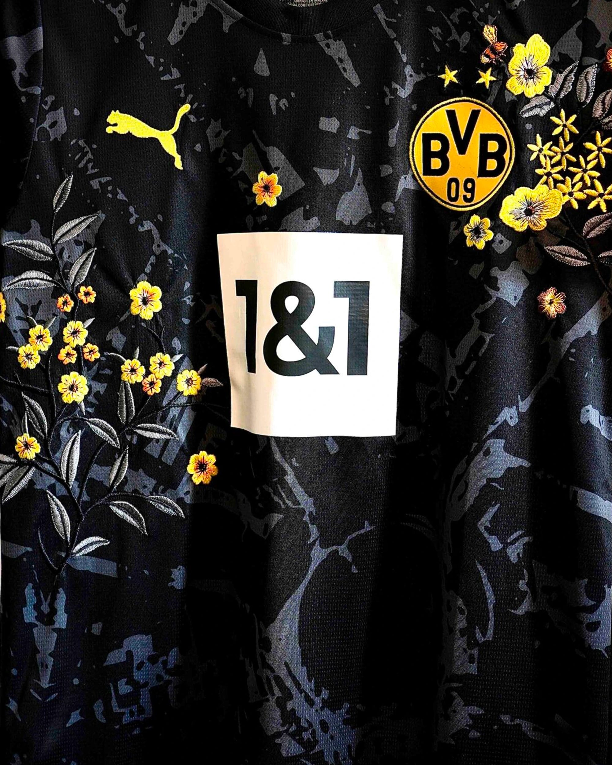 Close-up of the club crest on the Dortmund 'Yellow Bee' Edition Jersey 2022-23, beautifully framed by intricate floral art.