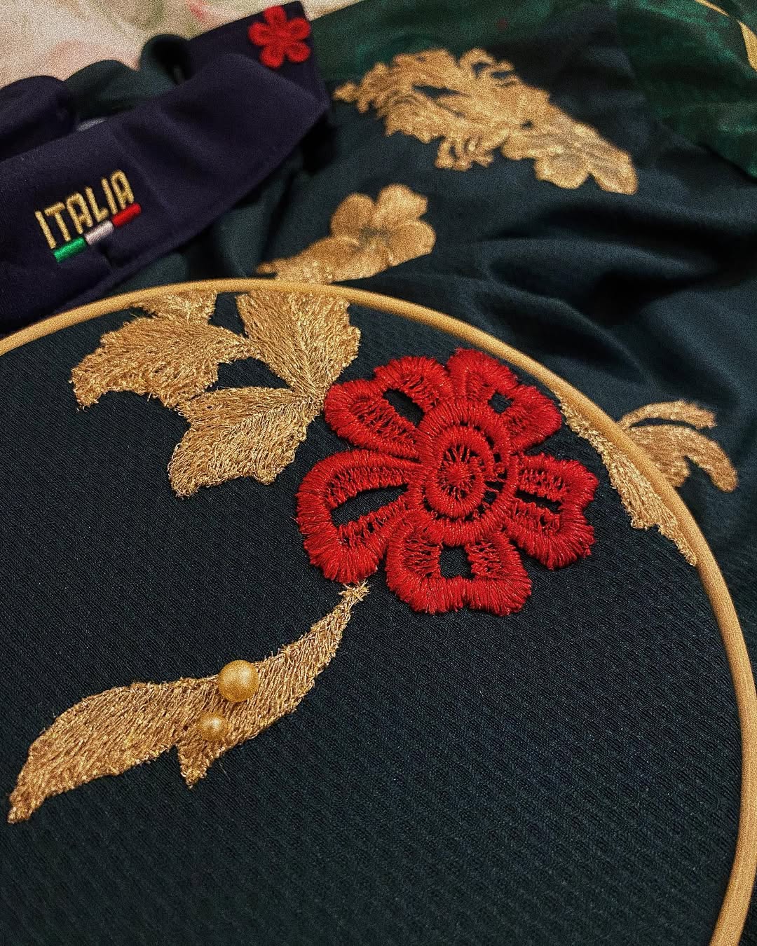 Close-up of hand-embroidered floral stitching on a football jersey, featuring red and gold thread details on dark fabric