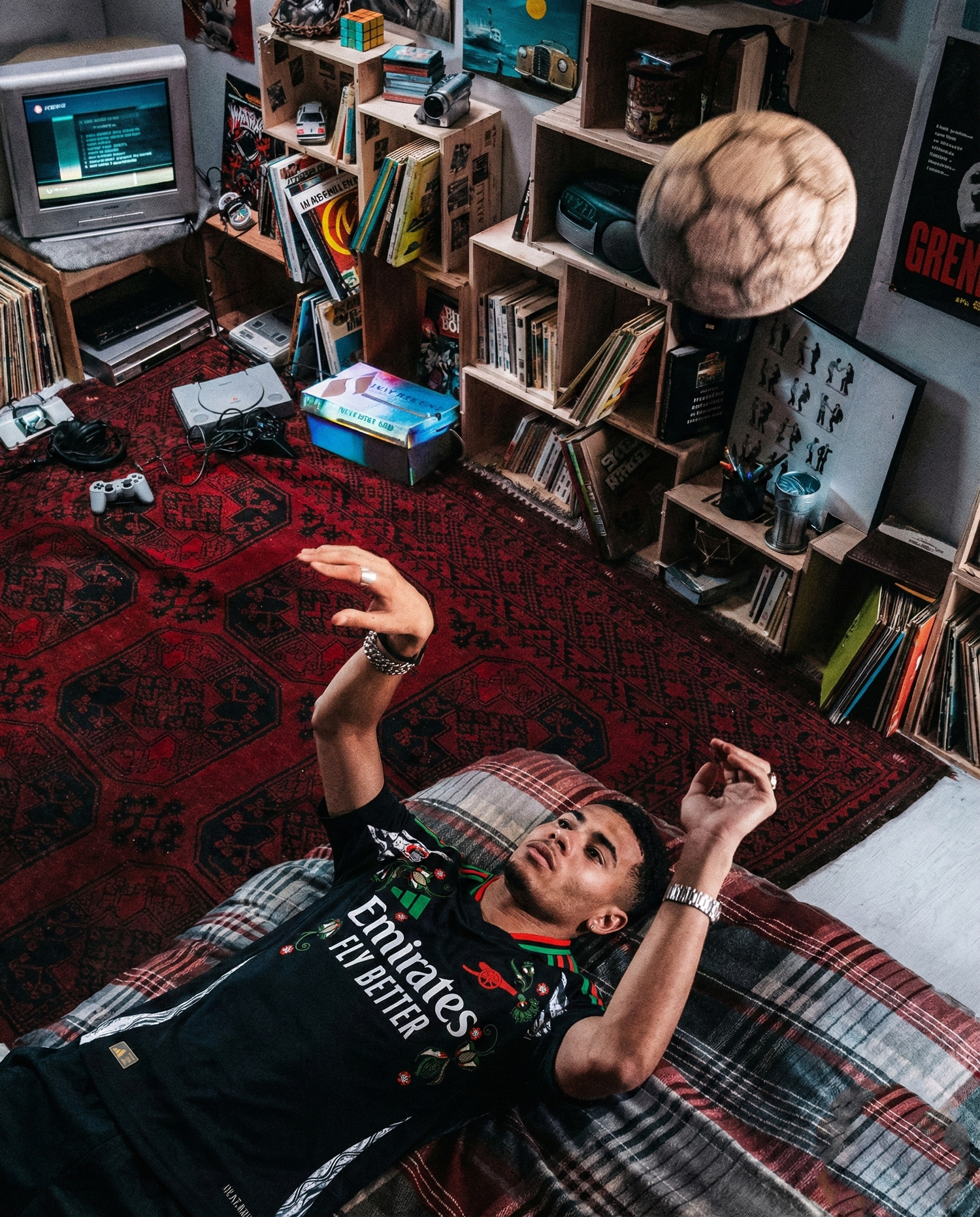 Male model wearing an embroidered football jersey, lying indoors in a vintage room with a football in motion