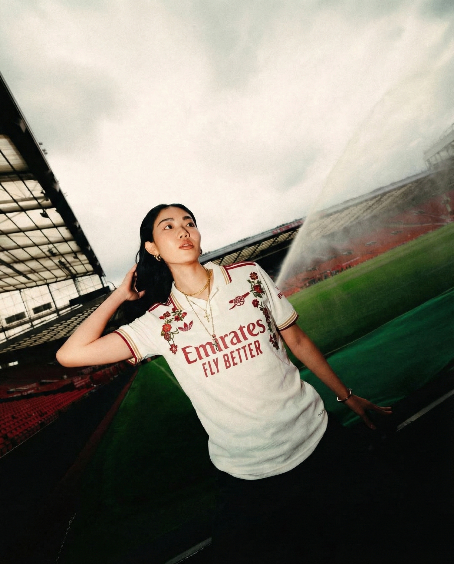 Female model wearing an embroidered football jersey, standing on a football stadium pitch
