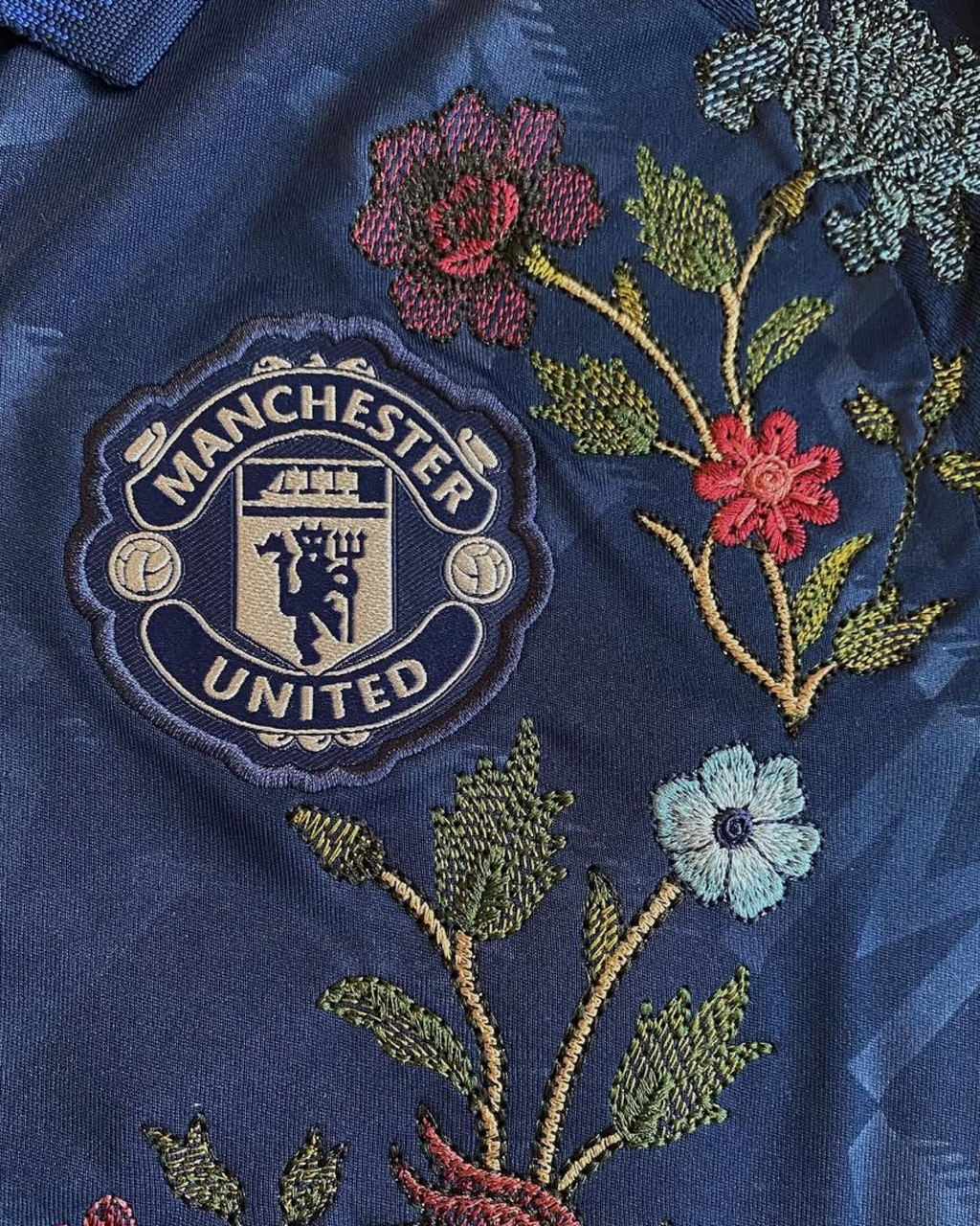 Embroidered Manchester United Away Jersey 2024-25 featuring floral embroidery and club logo on a navy background.