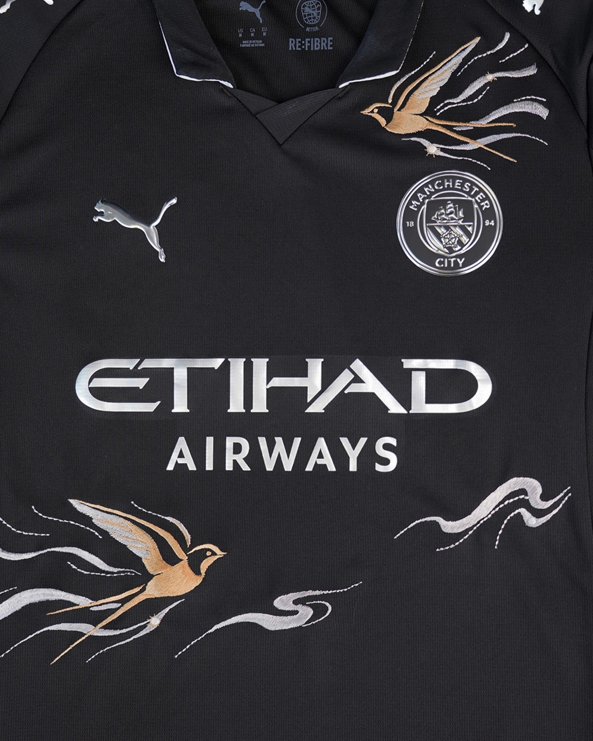 Close-up of the club crest on the Manchester City Embroidered Black Jersey, beautifully surrounded by intricate neon floral art.