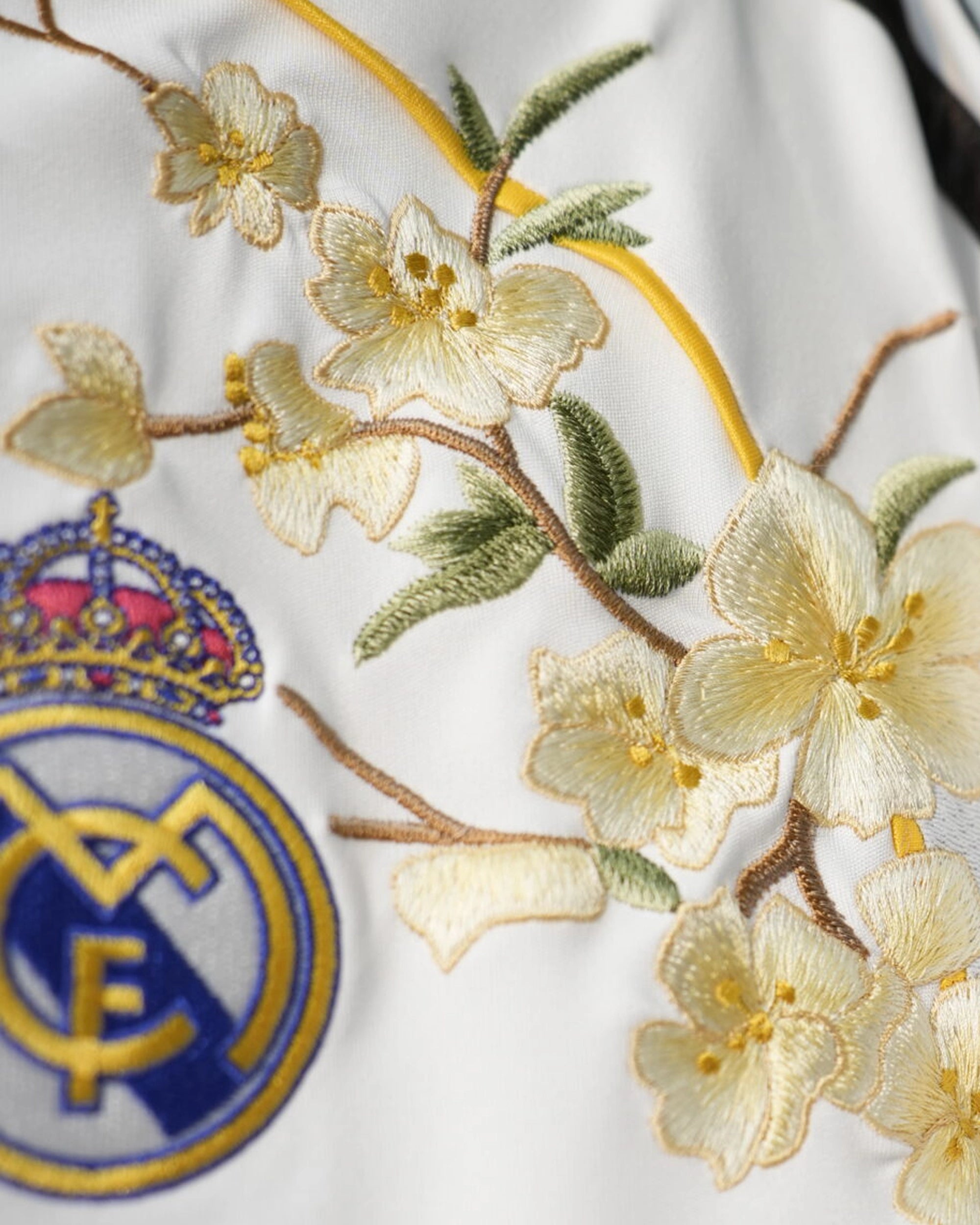 Detailed embroidery on the Real Madrid Embroidered Jersey highlighting the sports logo surrounded by intricate gold threadwork.