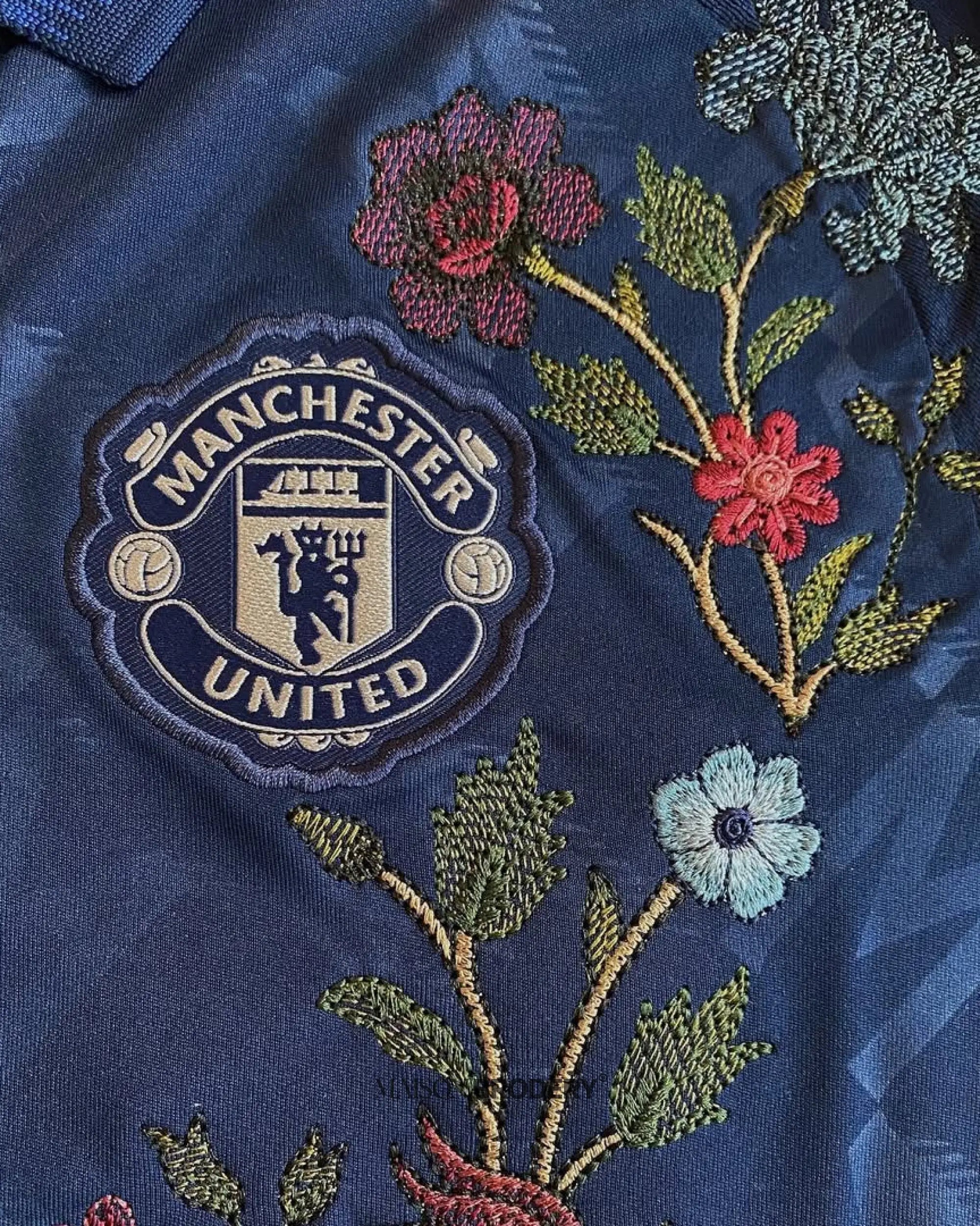 Embroidered Manchester United Away Jersey 2024-25 featuring intricate floral designs and team logo on a navy background.