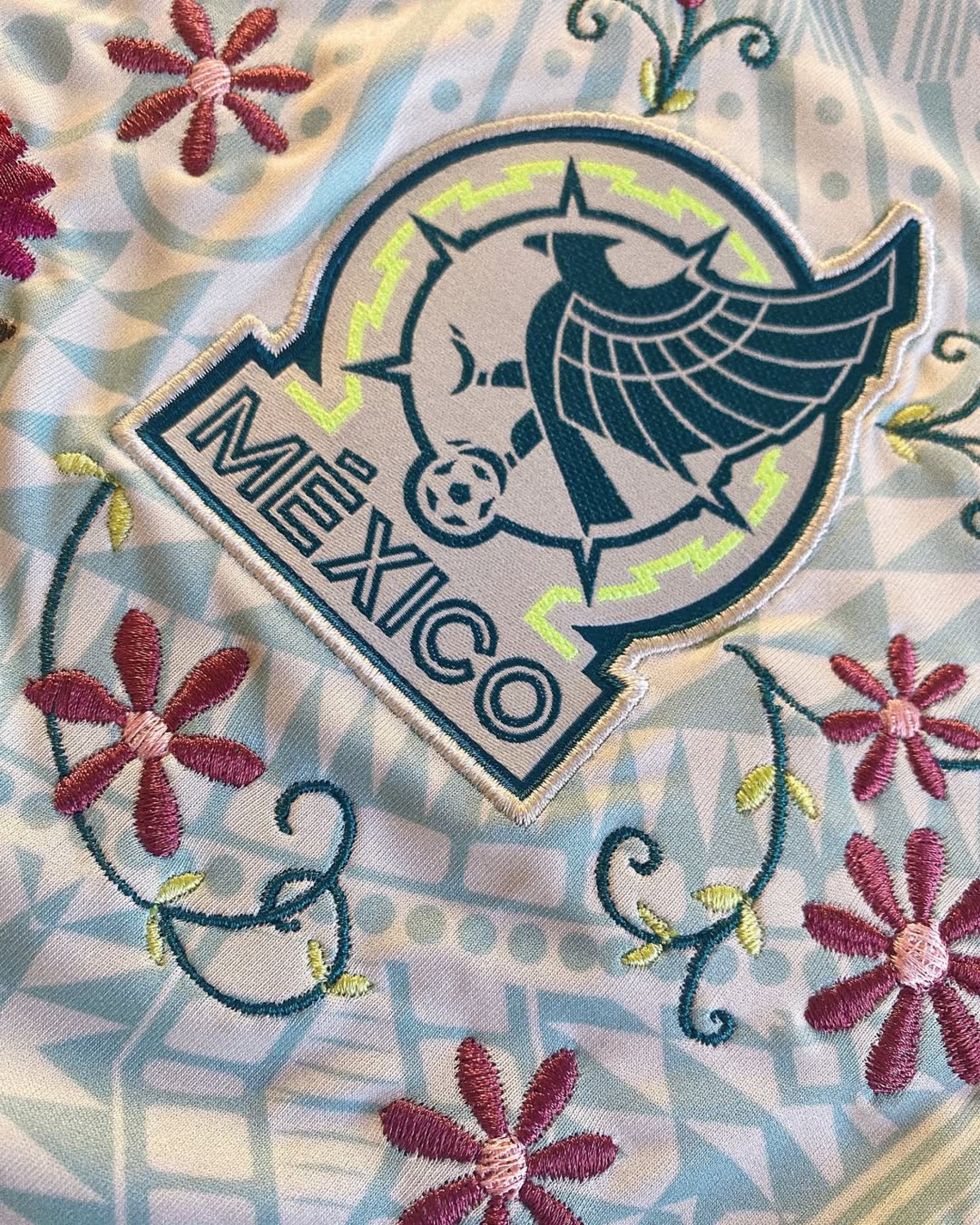 Close-up of the Newcastle United crest on the Embroidered Mexico Away Jersey 2024-25, surrounded by detailed monochromatic floral stitching.